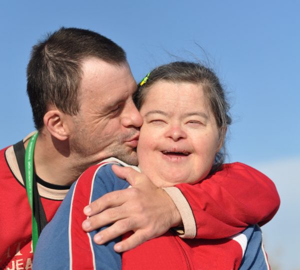 Two people with I/DD hugging and kissing. Two people with I/DD hugging and kissing.