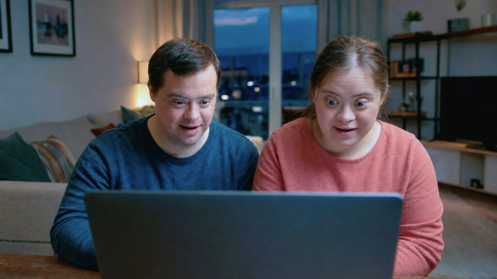 Two adults with Down syndrome viewing a laptop, illustrating pornography education for people with intellectual and developmental disabilities.